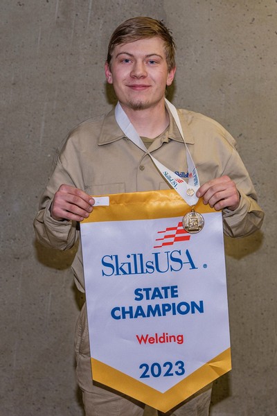 A student wears a gold medal and holds a championship banner.